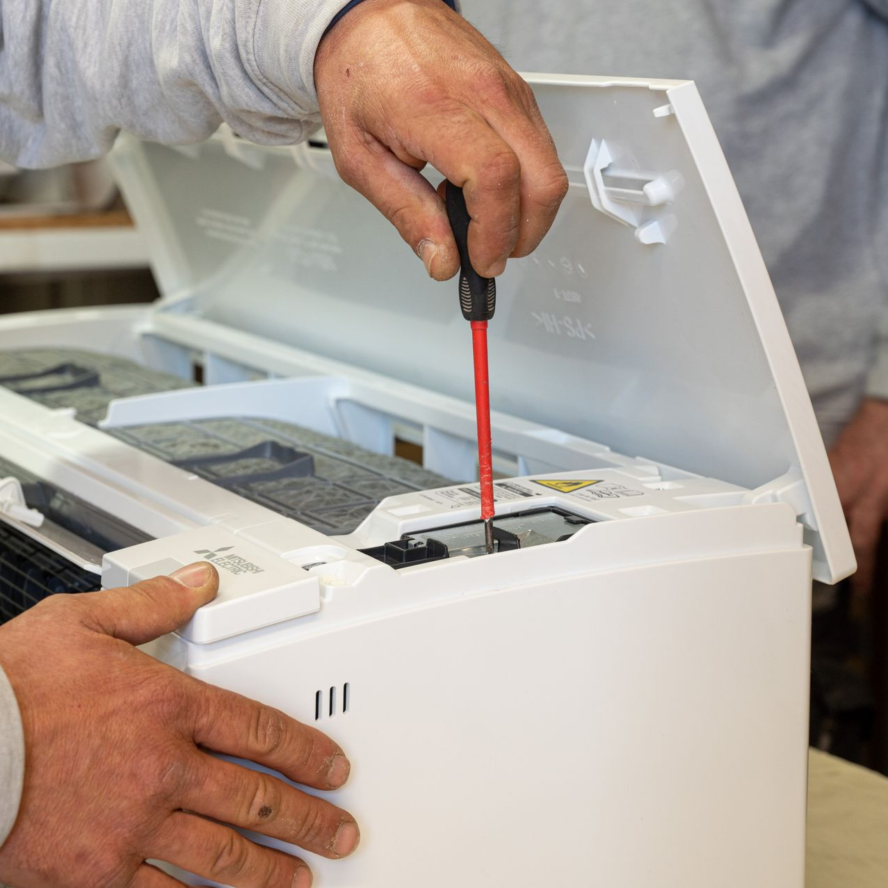Des mains qui utilisent un tournevis pour réparer un appareil blanc ouvert, dont les fils et les composants sont visibles.