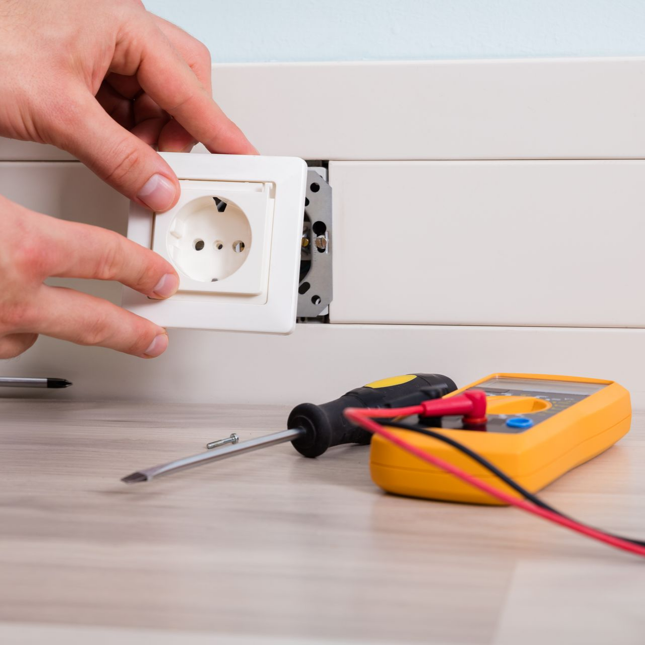 Installation manuelle d’une prise électrique blanche sur une table, avec un tournevis et un multimètre