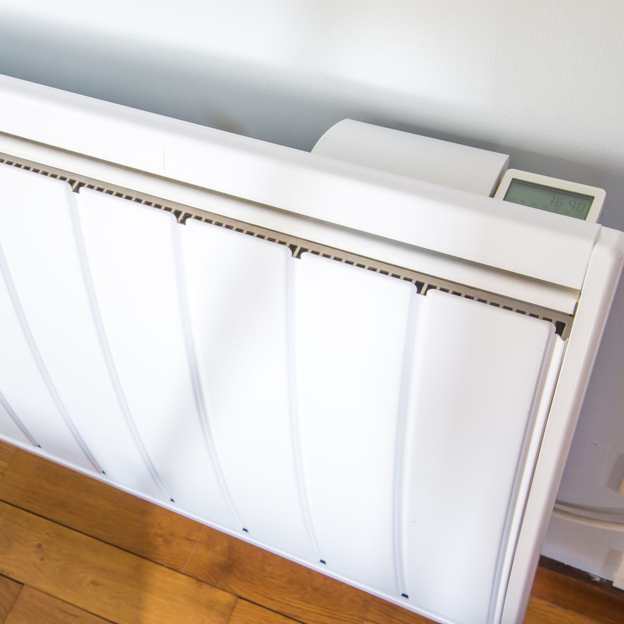 Radiateur blanc à côté d’un parquet, avec un petit thermostat qui dépasse sur le dessus