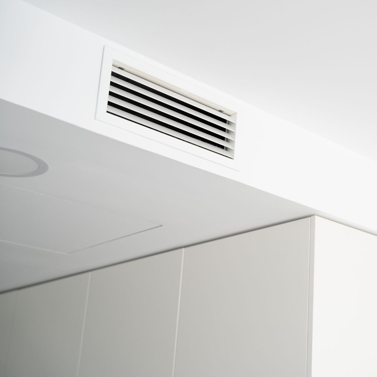 Bouche d’aération blanche au plafond, au-dessus d’un mur gris dans un intérieur moderne