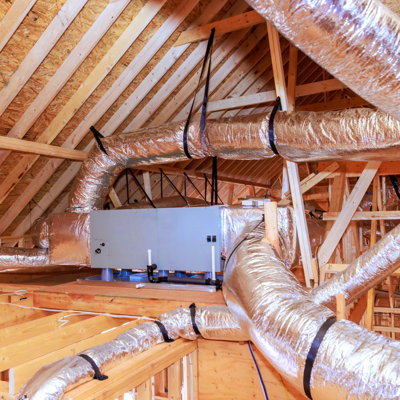 Combles avec poutres apparentes et conduits de ventilation en métal argenté isolés courant sous le plafond