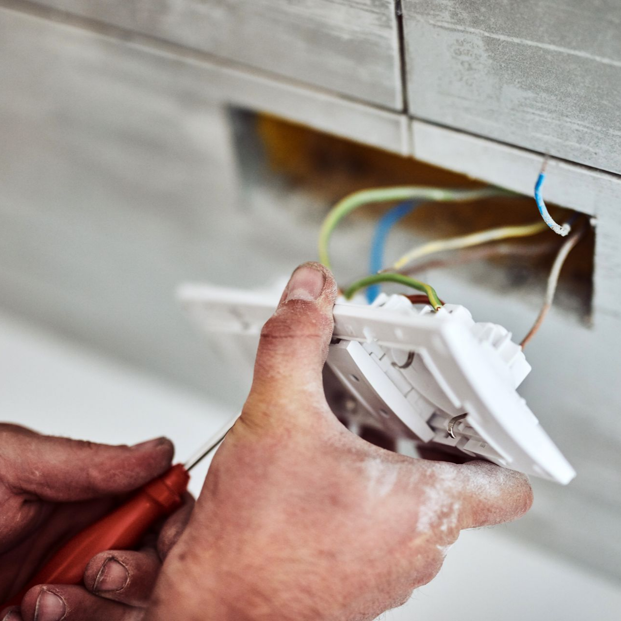 Des mains raccordent une prise électrique blanche dans une ouverture murale, avec des outils à proximité.