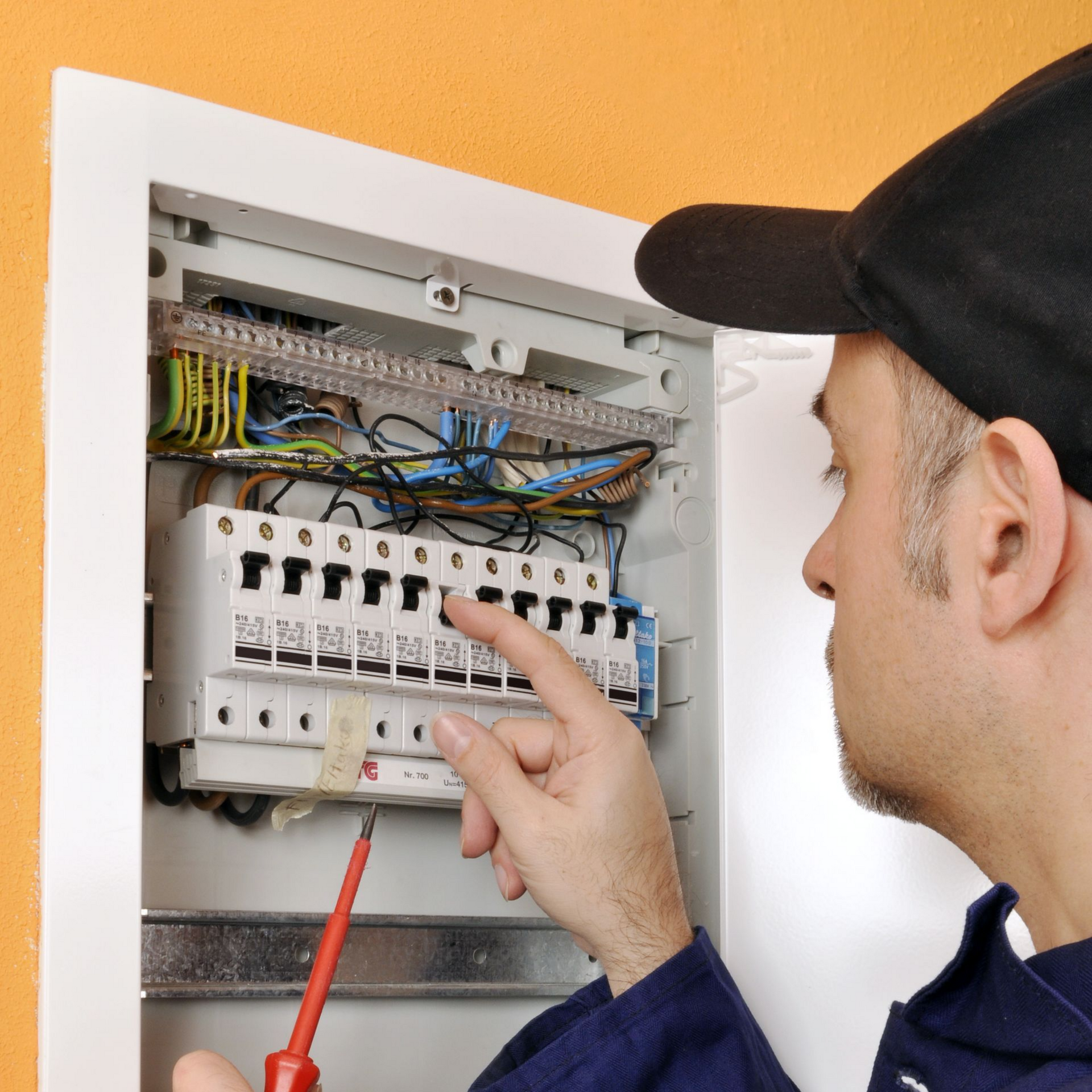 Un électricien inspecte un tableau électrique à l’aide d’un testeur de tension, dans un coffret électrique ouvert
