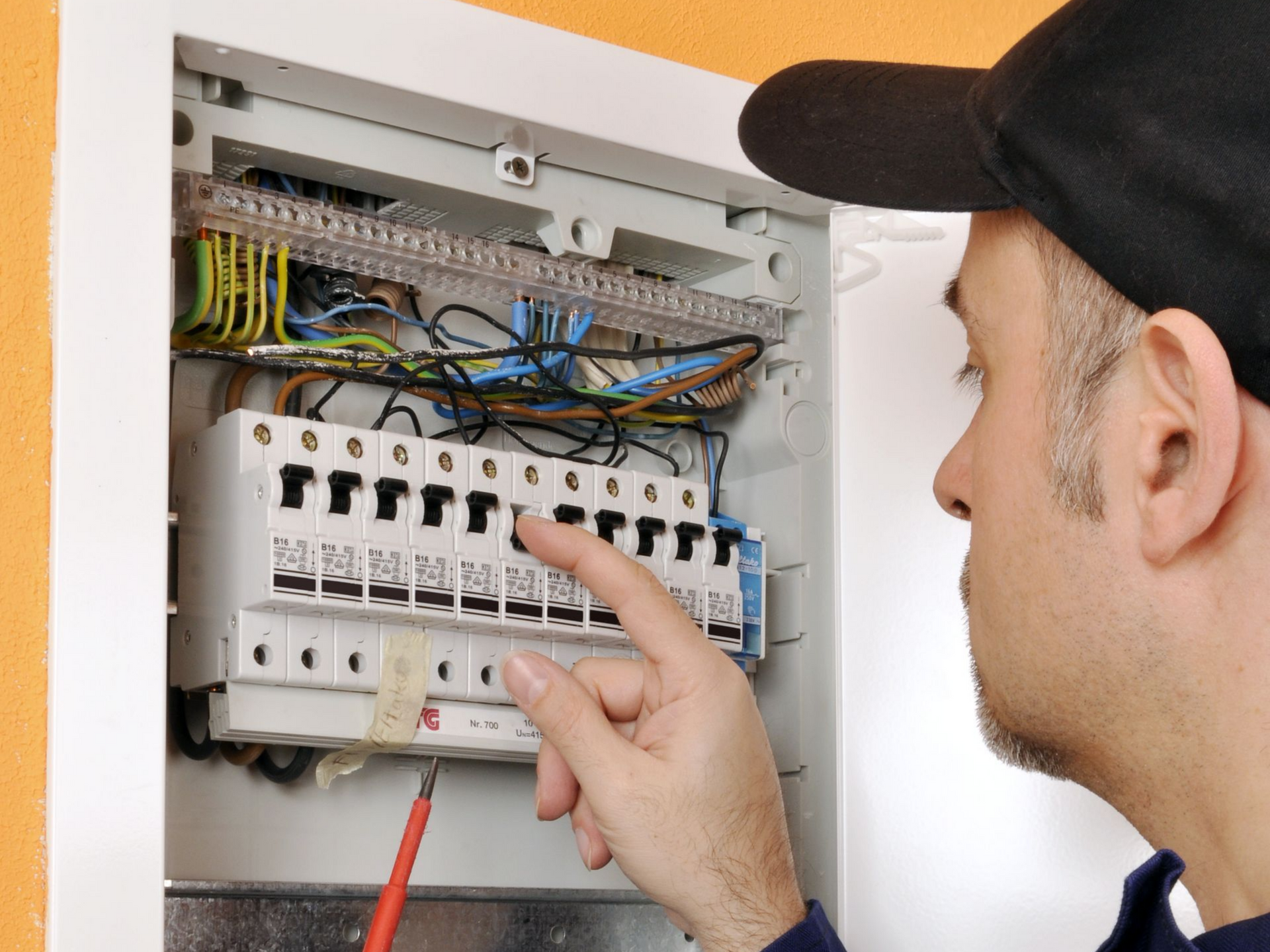 Technicien inspectant un tableau électrique ouvert avec des fils et des interrupteurs apparents