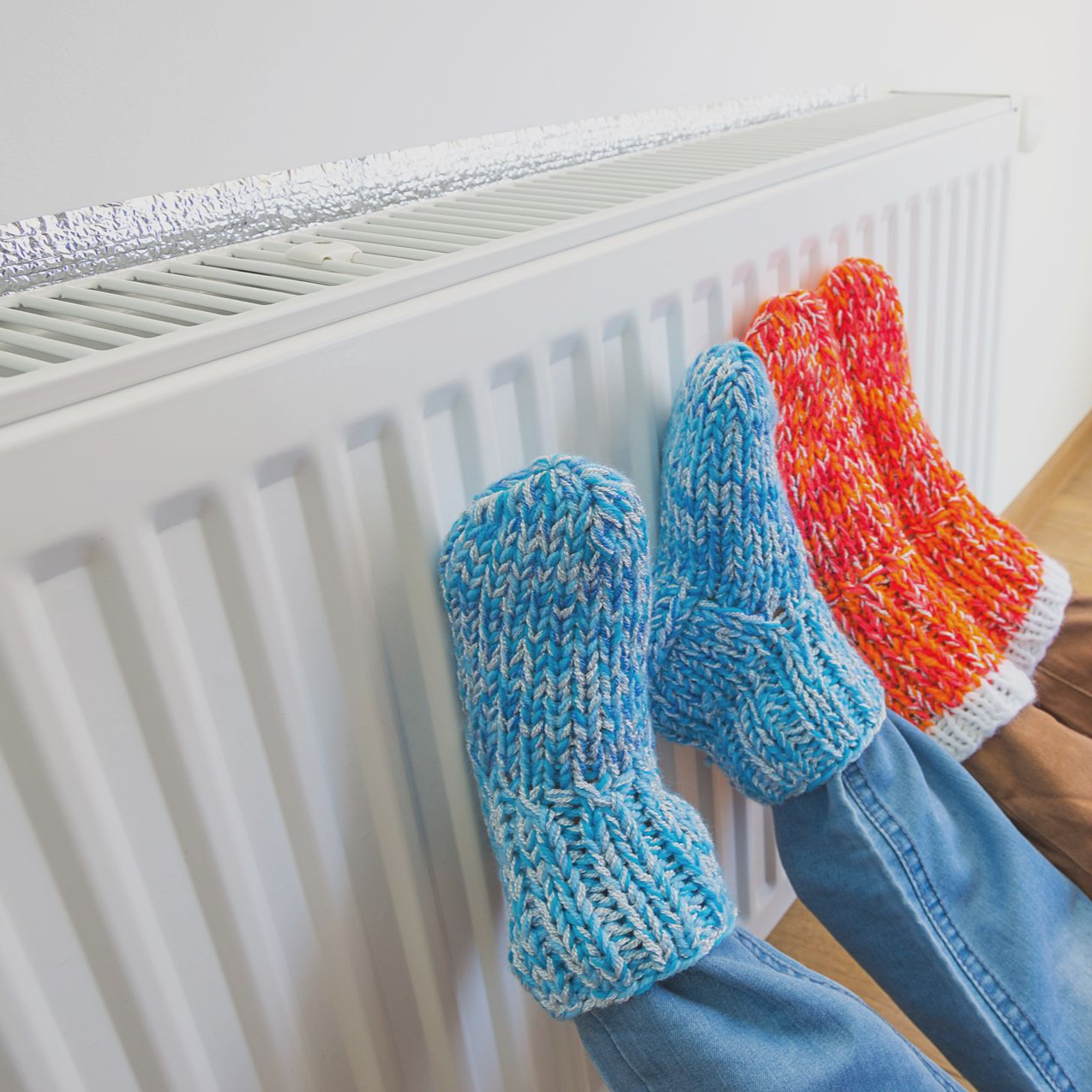 Des pieds vêtus de chaussettes en maille bleues, orange et rouges suspendues à un radiateur blanc pour apprécier la chaleur