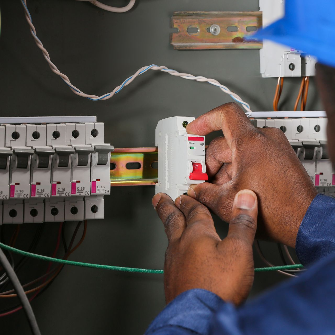 Électricien installant un disjoncteur dans un tableau électrique avec des fils dénudés