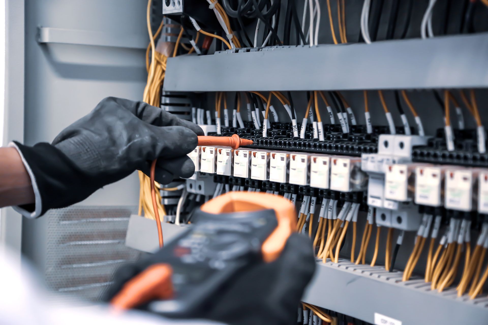 Technicien ganté raccordant un tableau de commande électrique avec des câbles orange et noirs