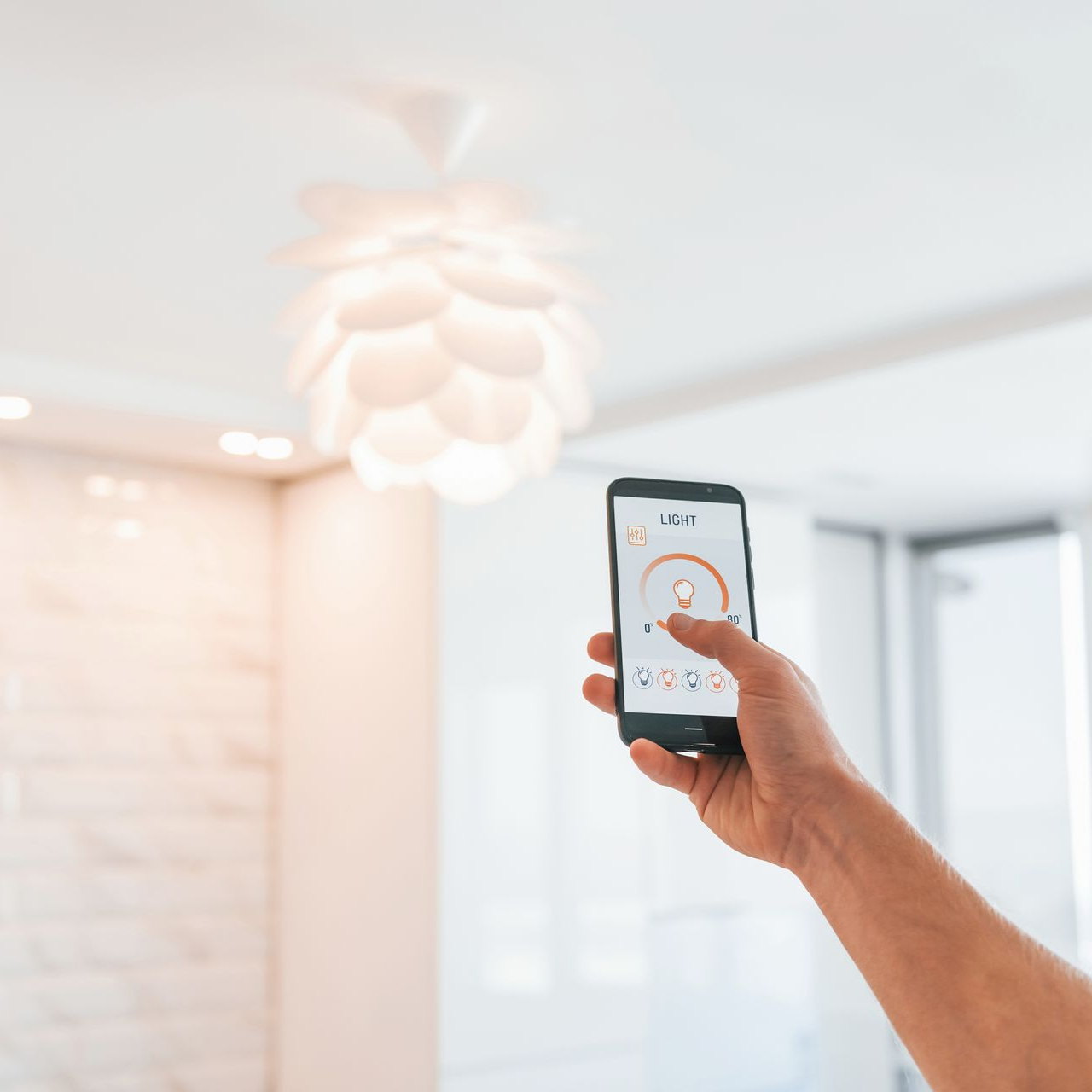 Une main tenant un smartphone pour contrôler un plafonnier lumineux dans une pièce moderne
