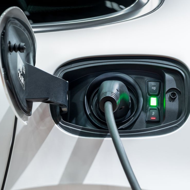 Prise de recharge d’une voiture électrique avec le câble branché et des voyants verts allumés sur un véhicule blanc.