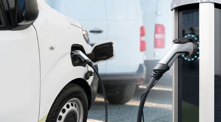 Voiture électrique blanche en charge à une borne, avec une autre camionnette garée en arrière-plan
