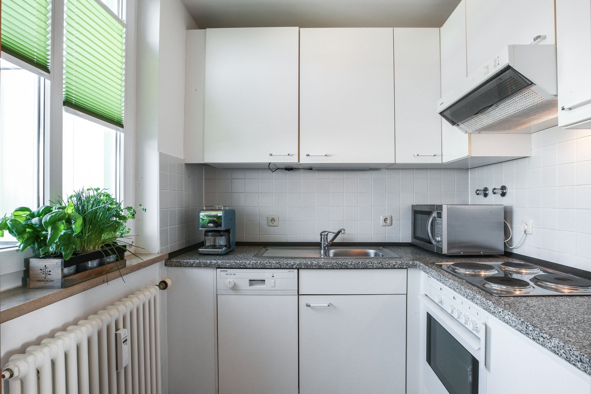 A kitchen with white cabinets , a sink , a microwave , and a window.