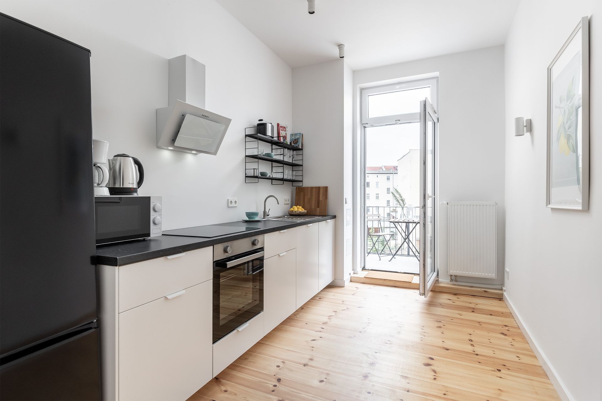 A kitchen with white cabinets , a black refrigerator , a black stove top oven , and a wooden floor.