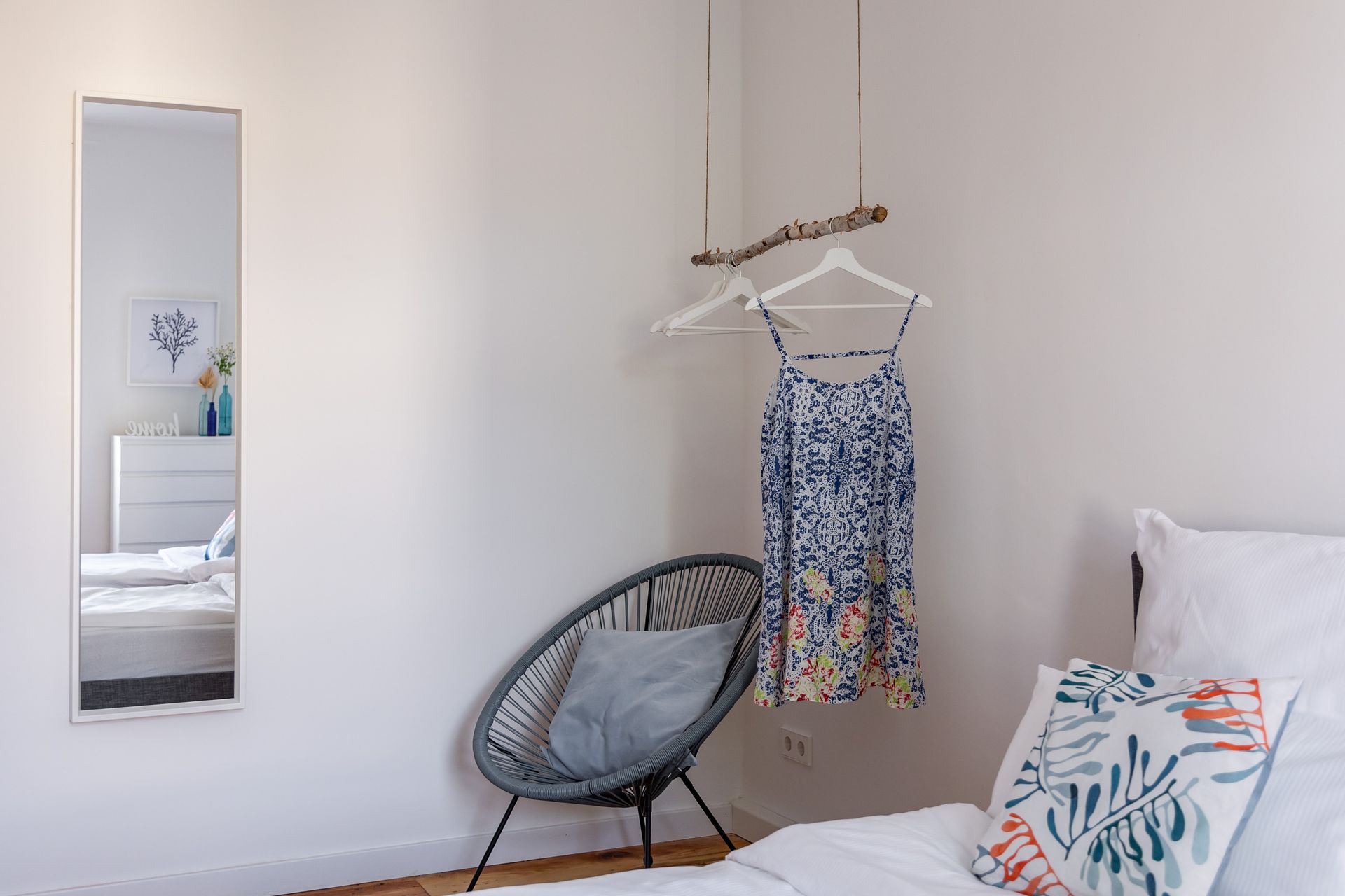 A bedroom with a bed , chair , mirror and clothes hanging on a rack.