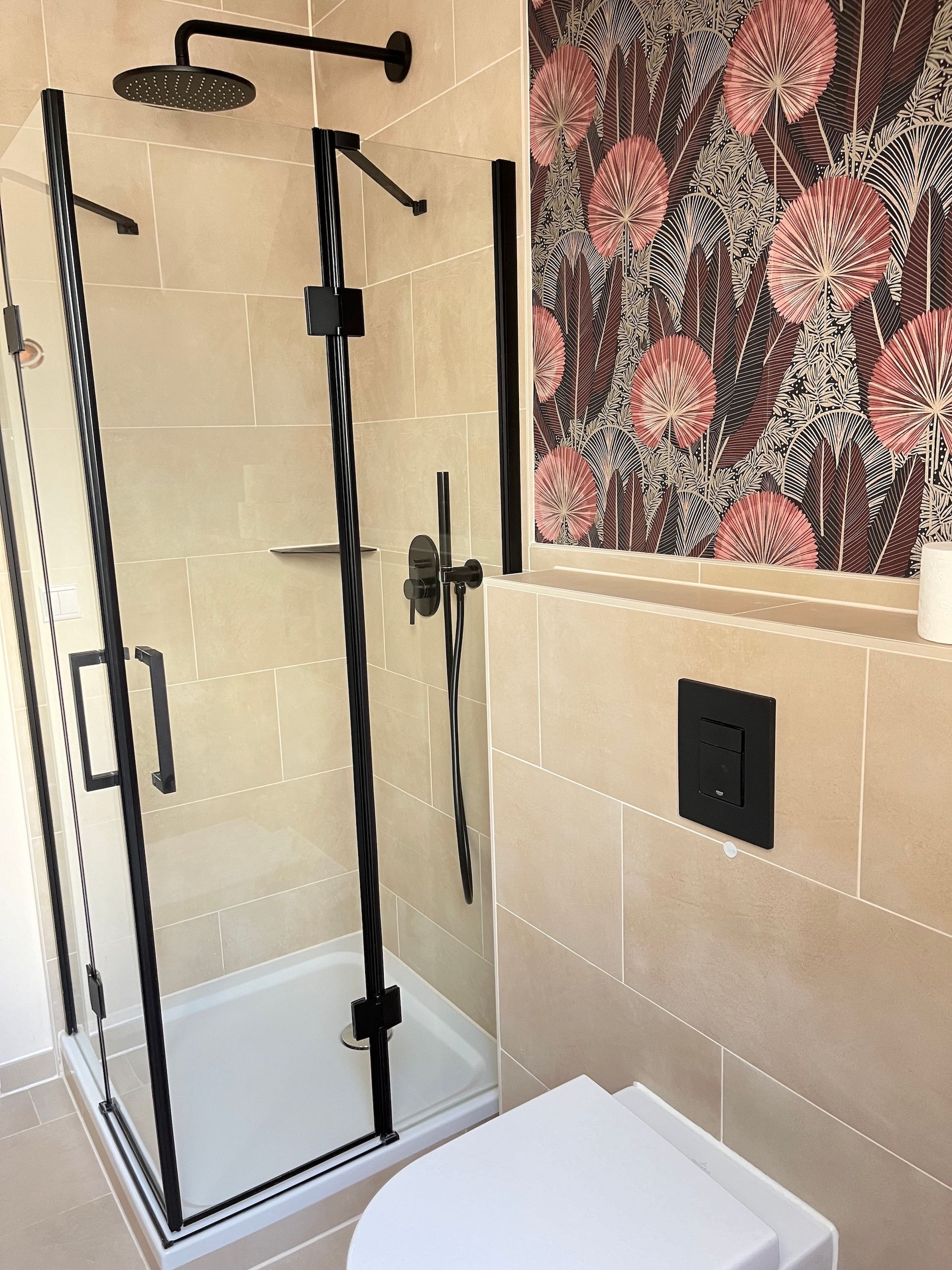 A bathroom with a toilet , shower , and floral wallpaper.