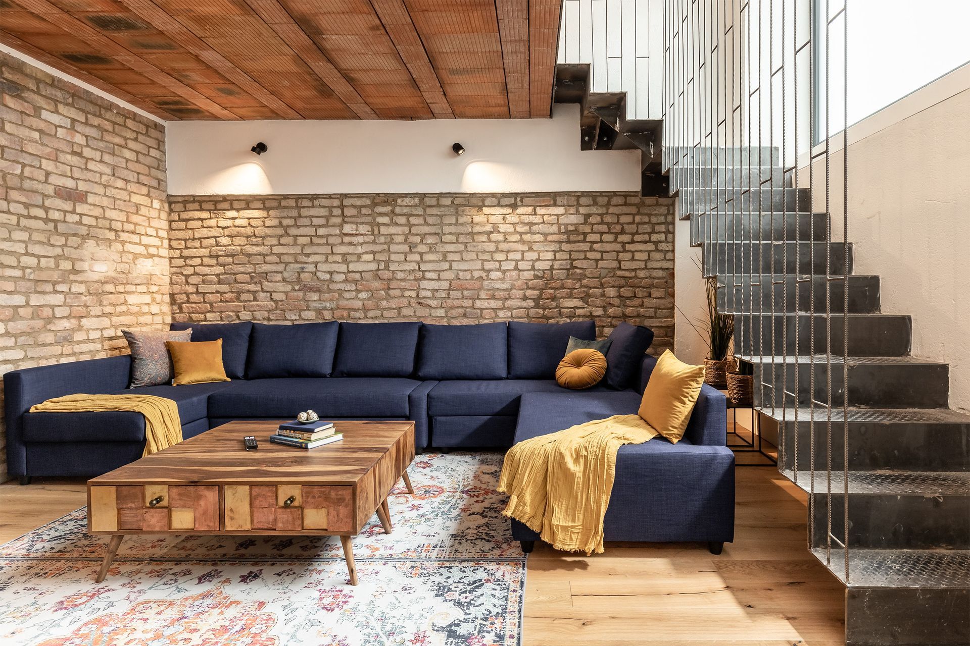 A living room with a blue sectional couch , coffee table , and stairs.