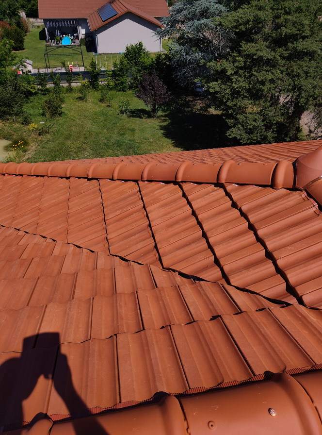 Vue du toit en tuiles de terre cuite orange, avec une cour, des arbres et des maisons en contrebas.