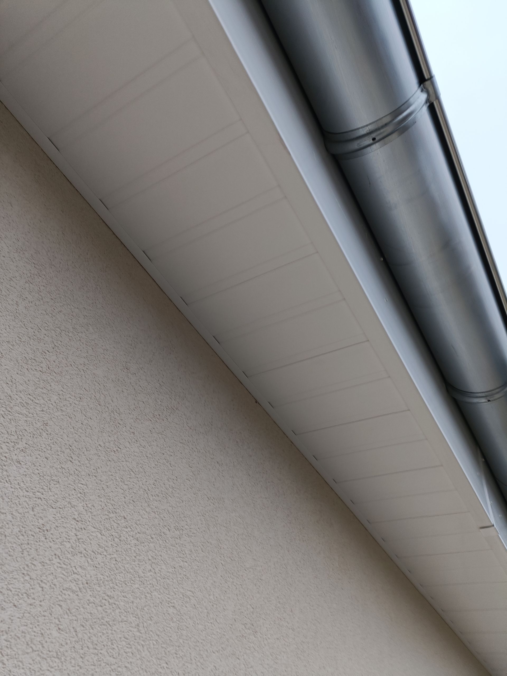 Gros plan sur le bord du toit d'un bâtiment avec soffite gris, gouttière et mur en stuc beige