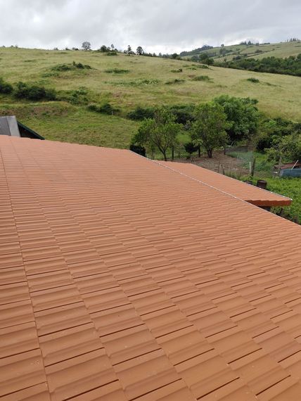 Toit de tuiles au premier plan, collines verdoyantes et ciel nuageux à l'arrière-plan.