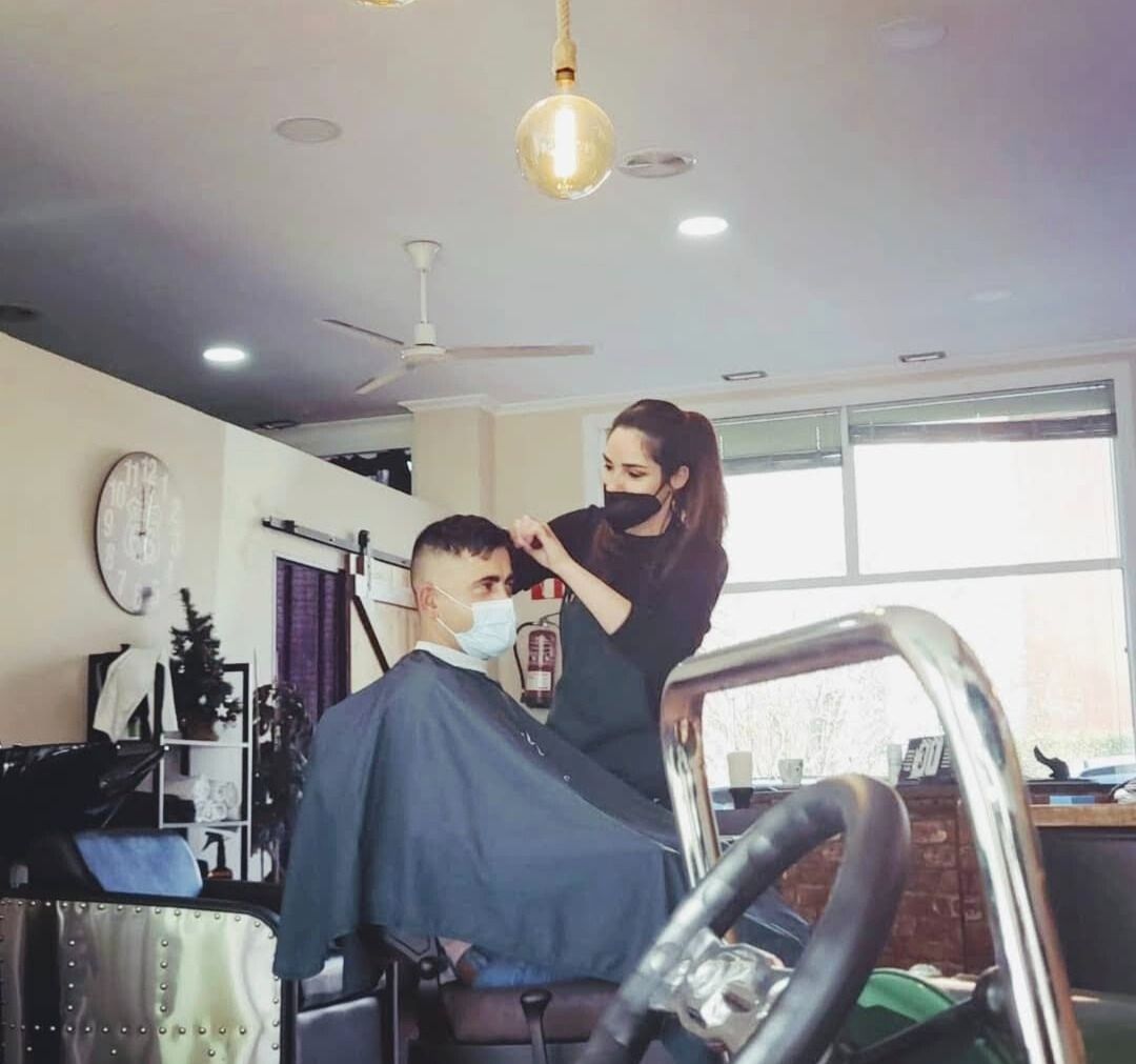 Una mujer está cortando el pelo a un hombre en una barbería.