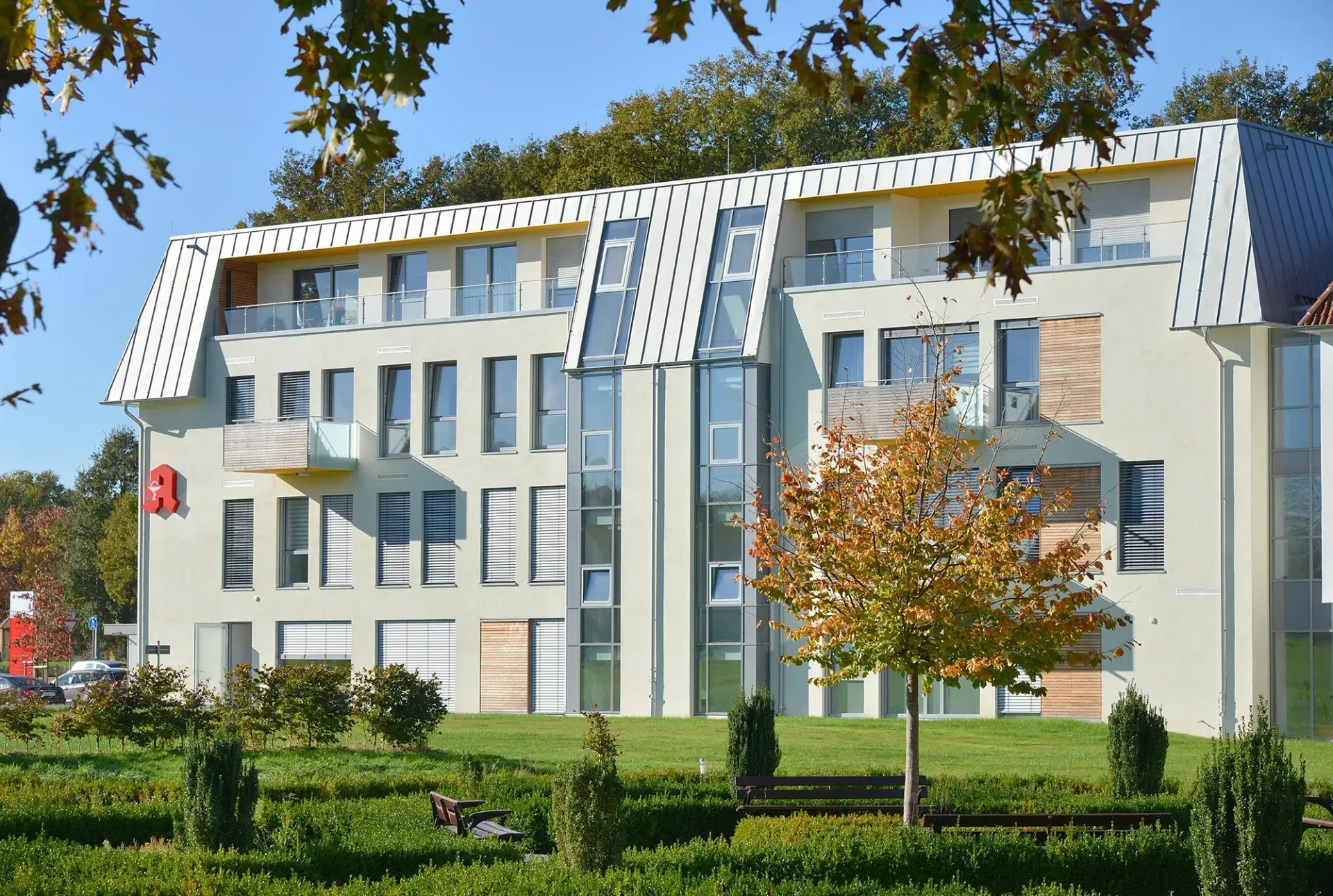 Ein großes Gebäude mit vielen Fenstern ist von Bäumen und Büschen umgeben