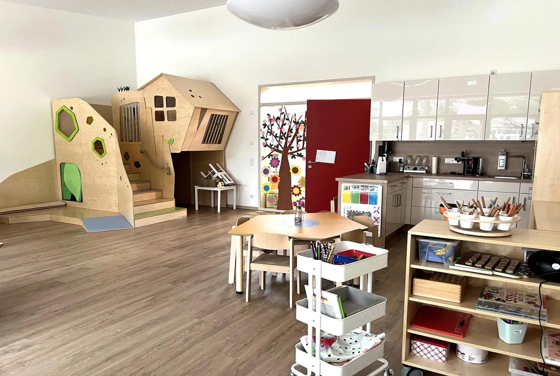 Ein Raum mit einem Holzspielhaus, Tischen und Stühlen.