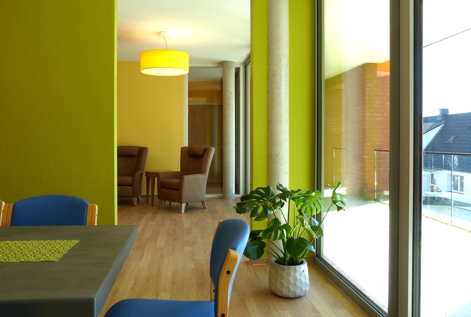 Ein Raum mit einem Tisch und Stühlen und einer Topfpflanze vor einem Fenster.