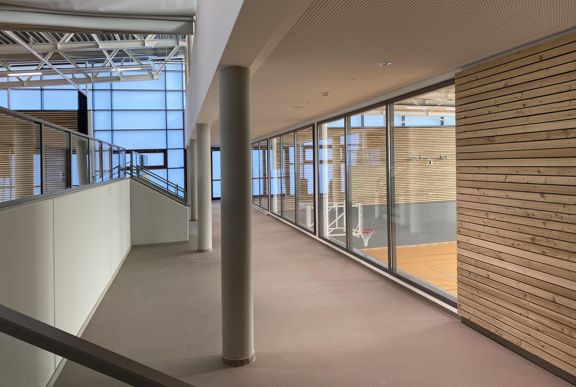 Ein langer Flur in einem Gebäude mit einem Basketballplatz im Hintergrund.