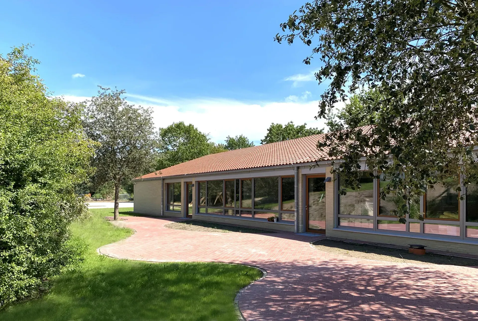 Ein großes Gebäude mit einem roten Ziegeldach ist von Bäumen und Gras umgeben.