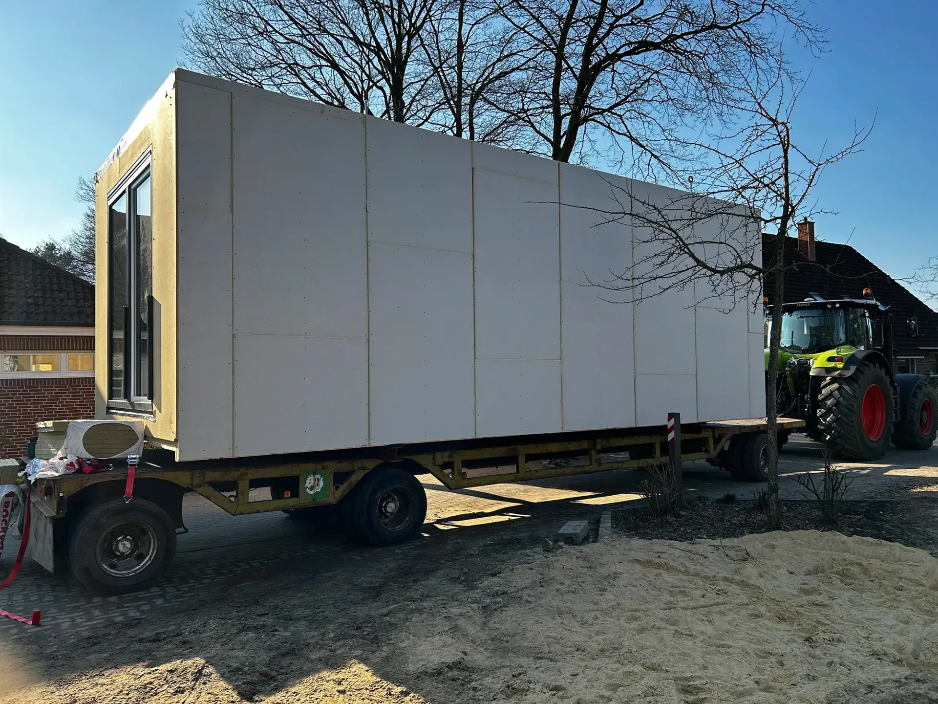 Ein Traktor transportiert eine große weiße Kiste auf einem Anhänger.