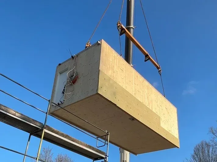 Eine große Holzkiste wird von einem Kran angehoben.