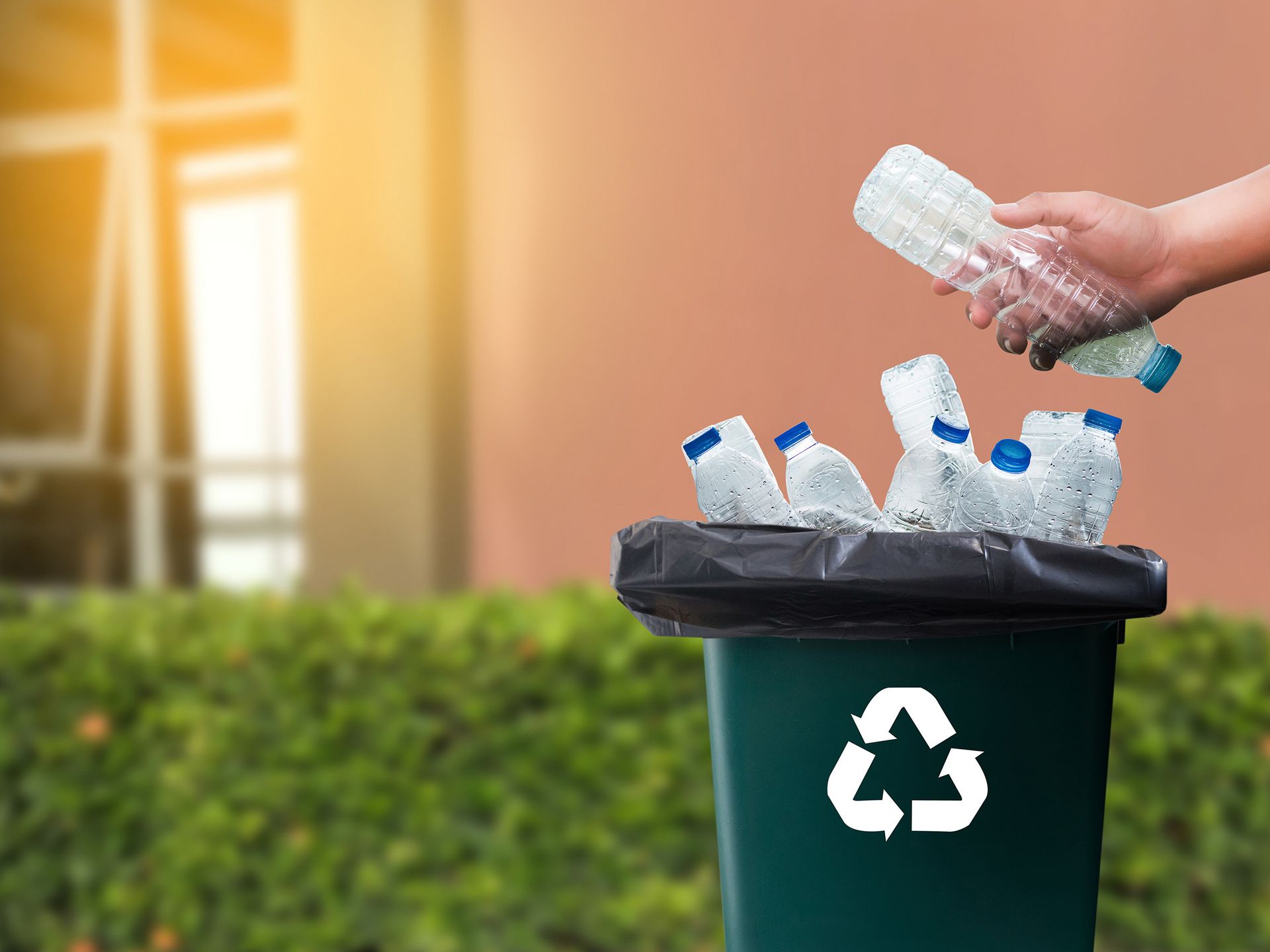 Una persona está tirando una botella de plástico a un contenedor de reciclaje.