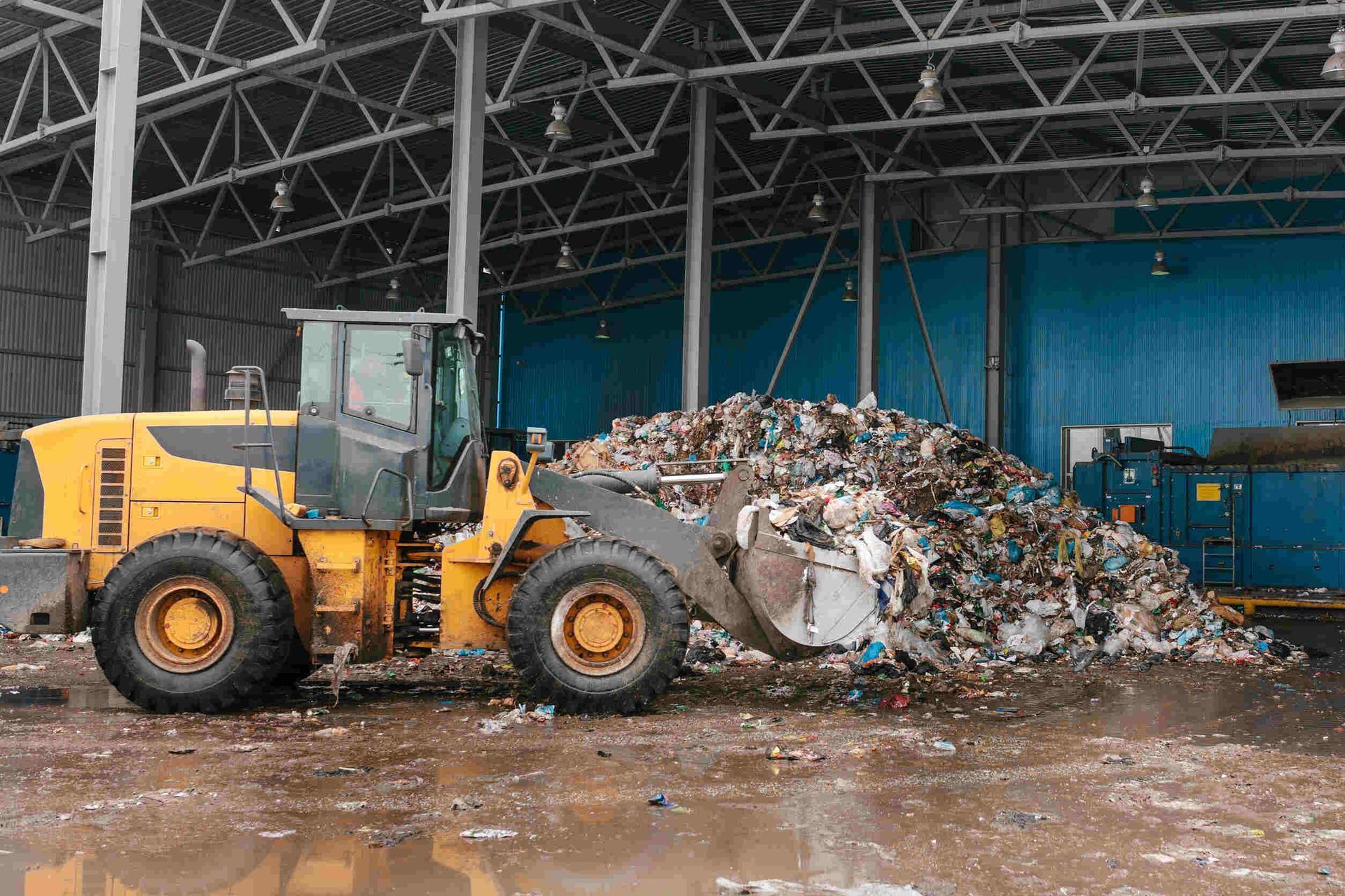 Una excavadora está cargando una pila de basura en un almacén.