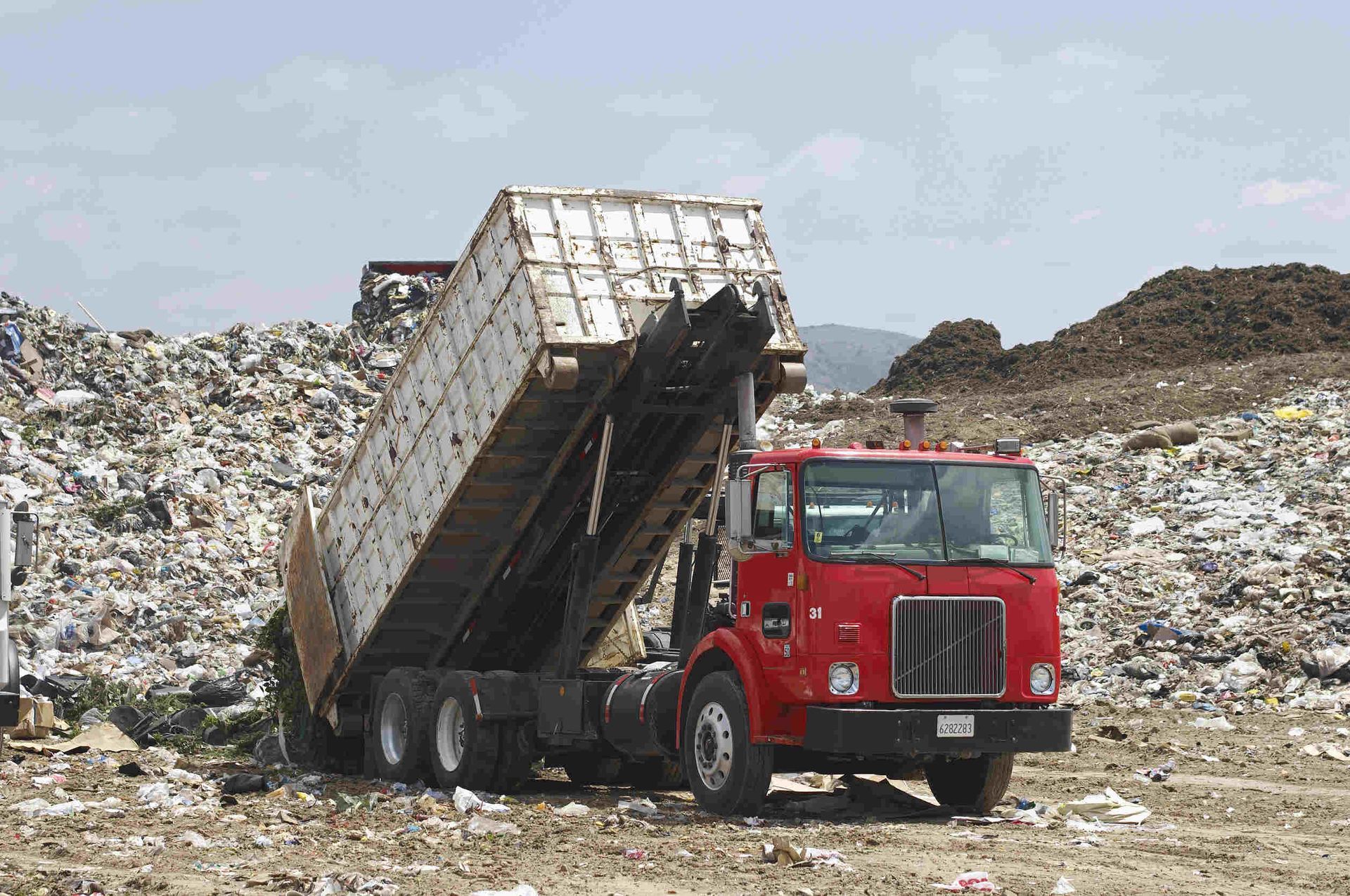 Un camión volquete rojo avanza a través de una pila de basura.