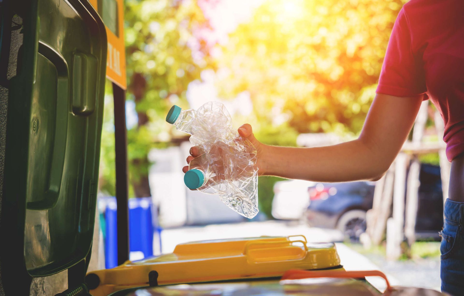 Una mujer está colocando una botella de plástico en un contenedor de reciclaje.