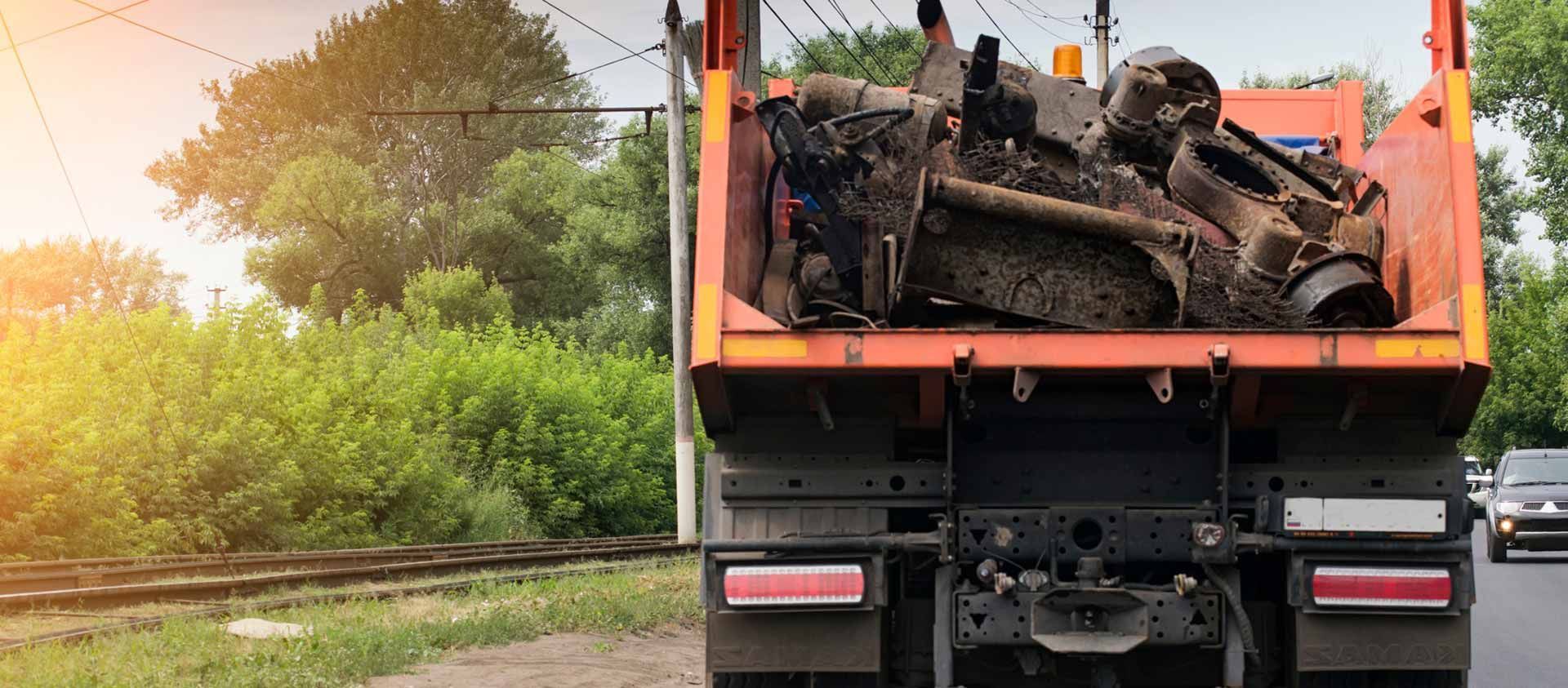 Un camión volquete lleva una gran pieza de metal en la parte trasera.