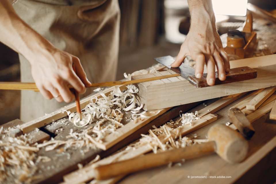 Ein Mann misst ein Stück Holz mit einem Maßband.