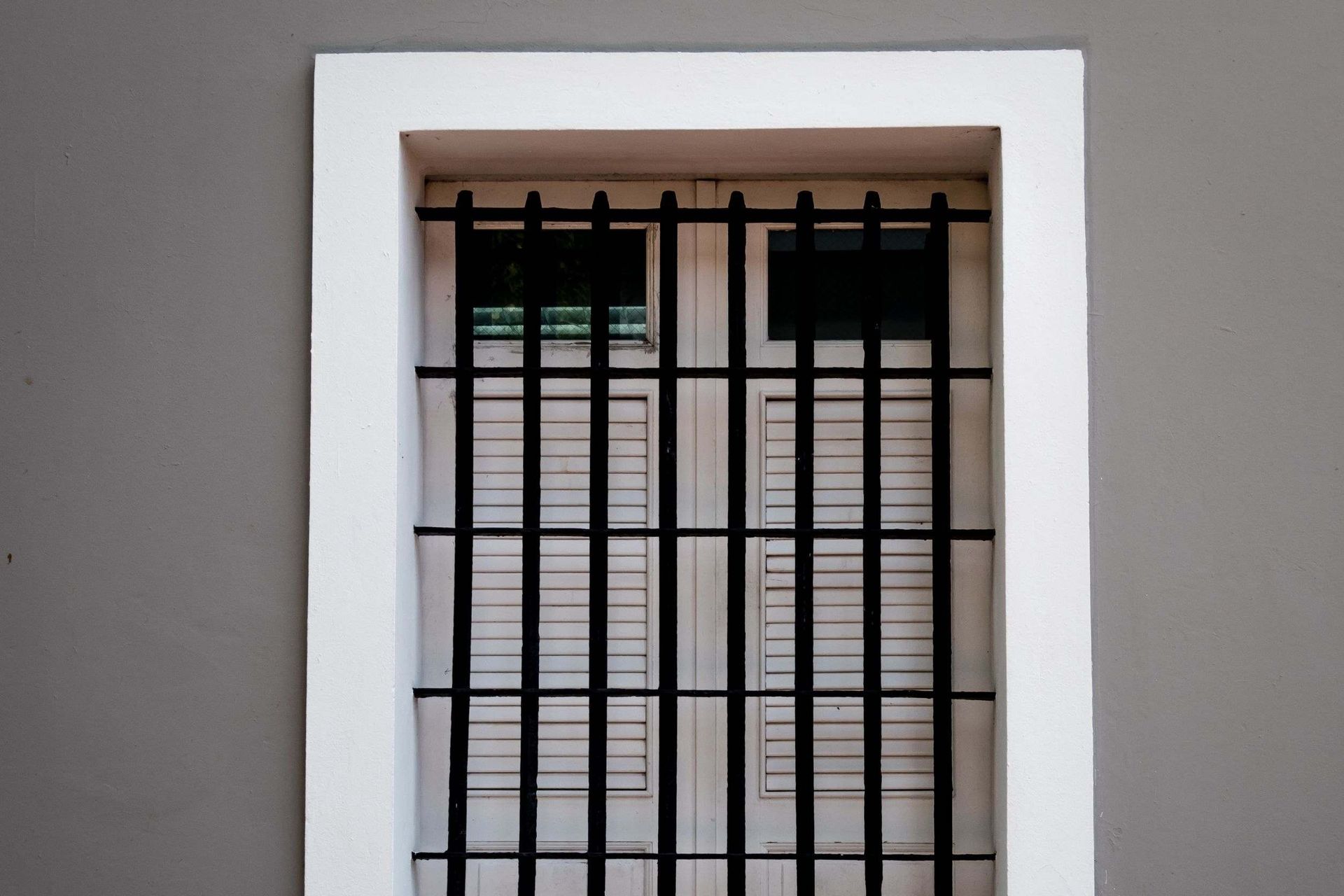 Ventana con rejas negras, marco blanco y pared gris.