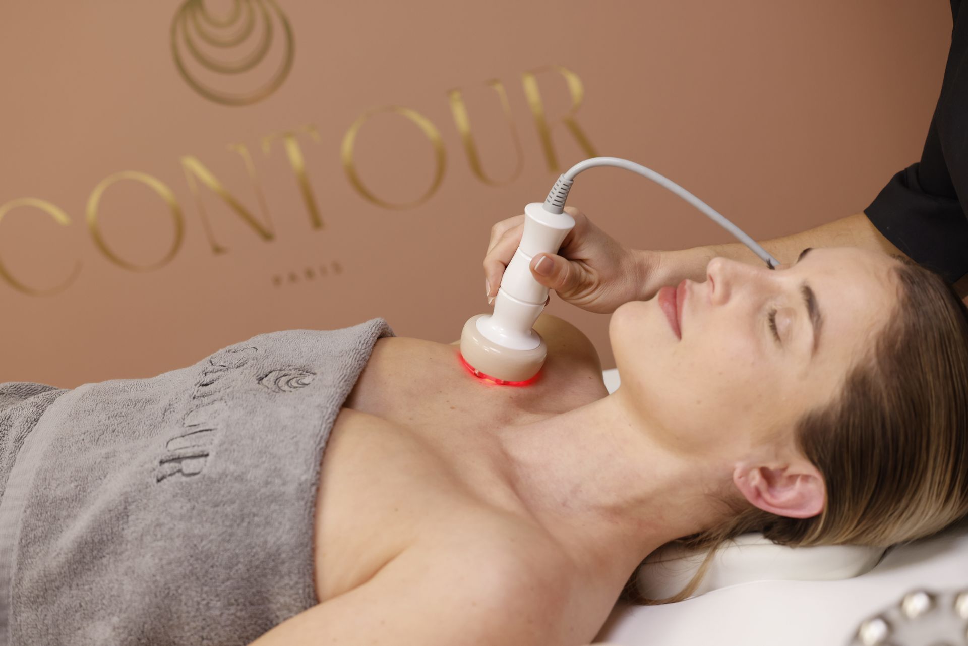 Une femme reçoit un traitement esthétique du cou à l'aide d'un appareil portatif dans un salon.