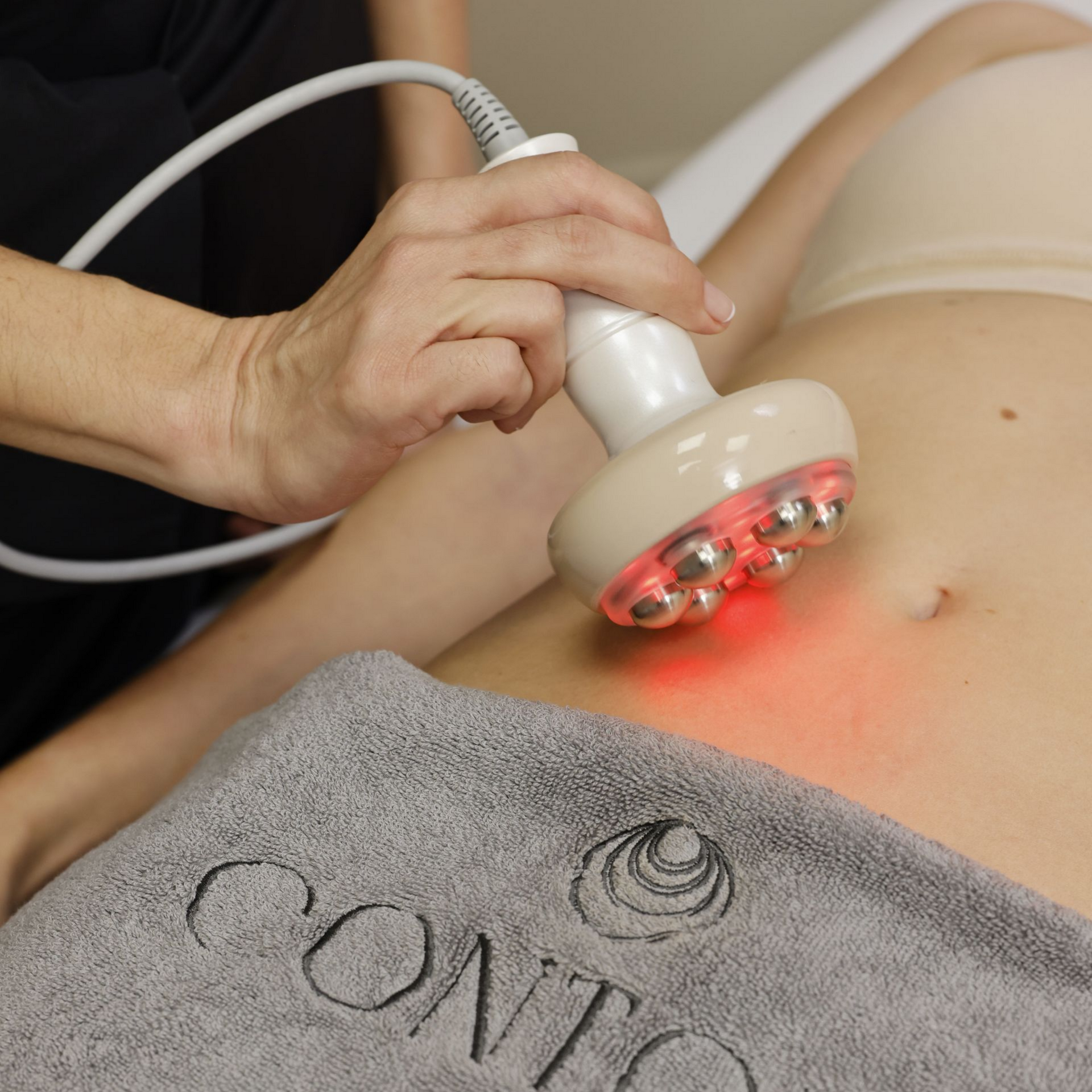 Une personne reçoit un traitement corporel avec un appareil à lumière rouge appliqué sur le ventre.