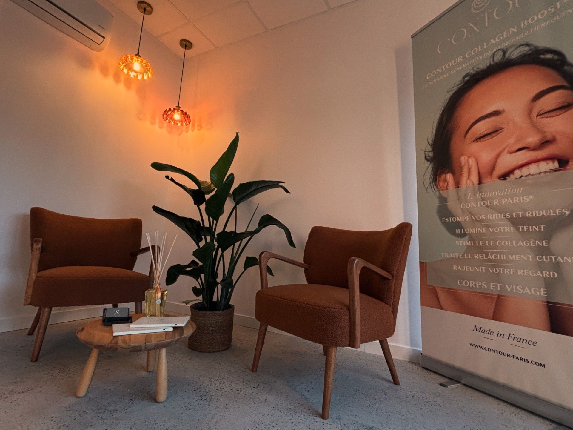 Coin d'attente confortable avec deux chaises marron, une plante en pot, une petite table et une publicité.