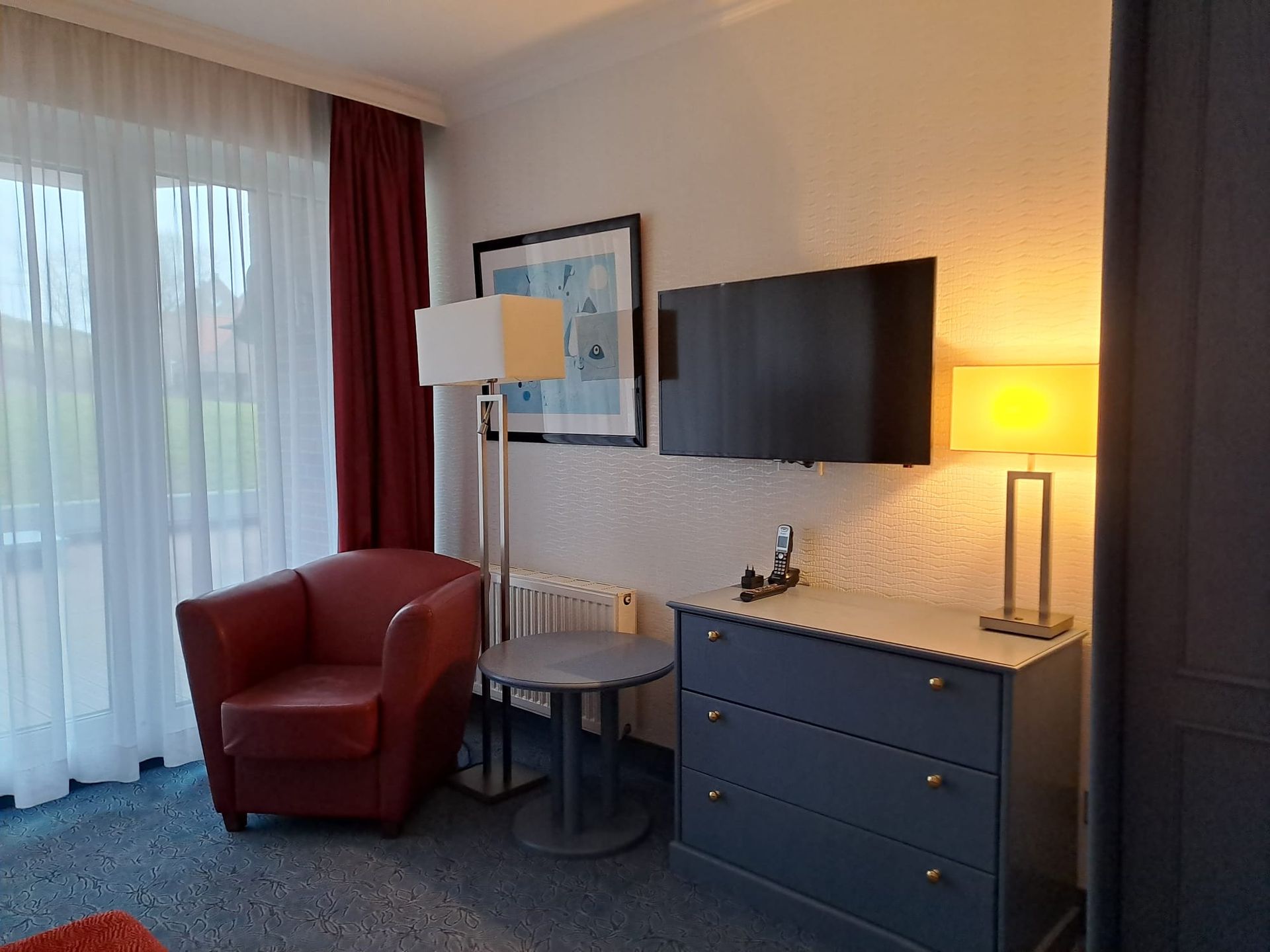 Ein Hotelzimmer mit Stuhl, Kommode, Tisch und Fernseher.