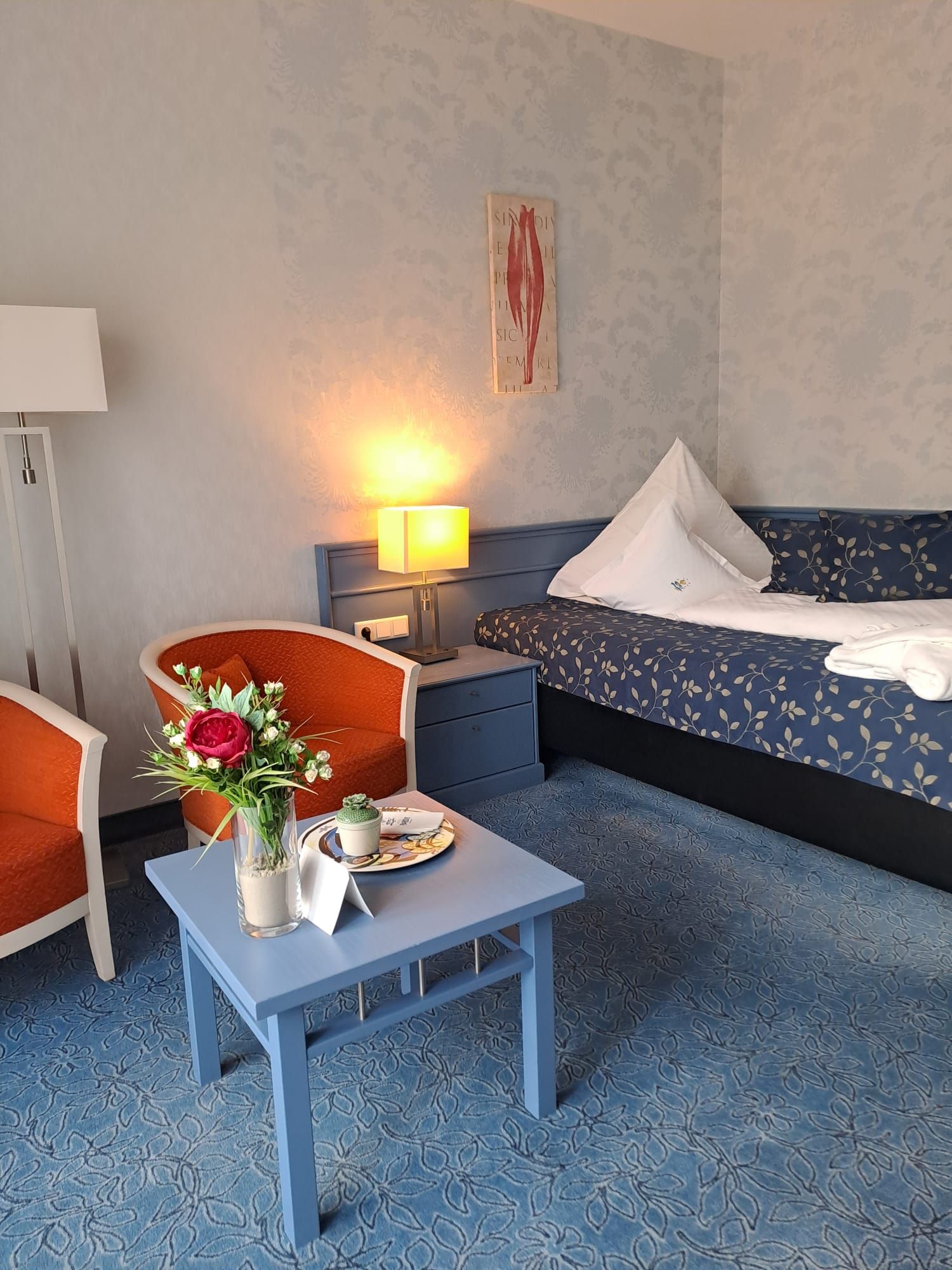 Ein Hotelzimmer mit einem Bett, Stühlen, einem Tisch und einer Vase mit Blumen.