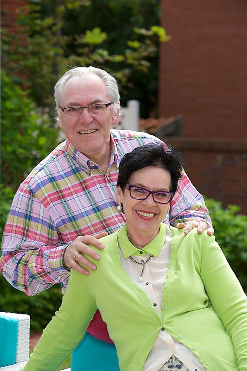 Ein Mann und eine Frau posieren für ein Foto. Die Frau trägt eine Brille und einen grünen Pullover.