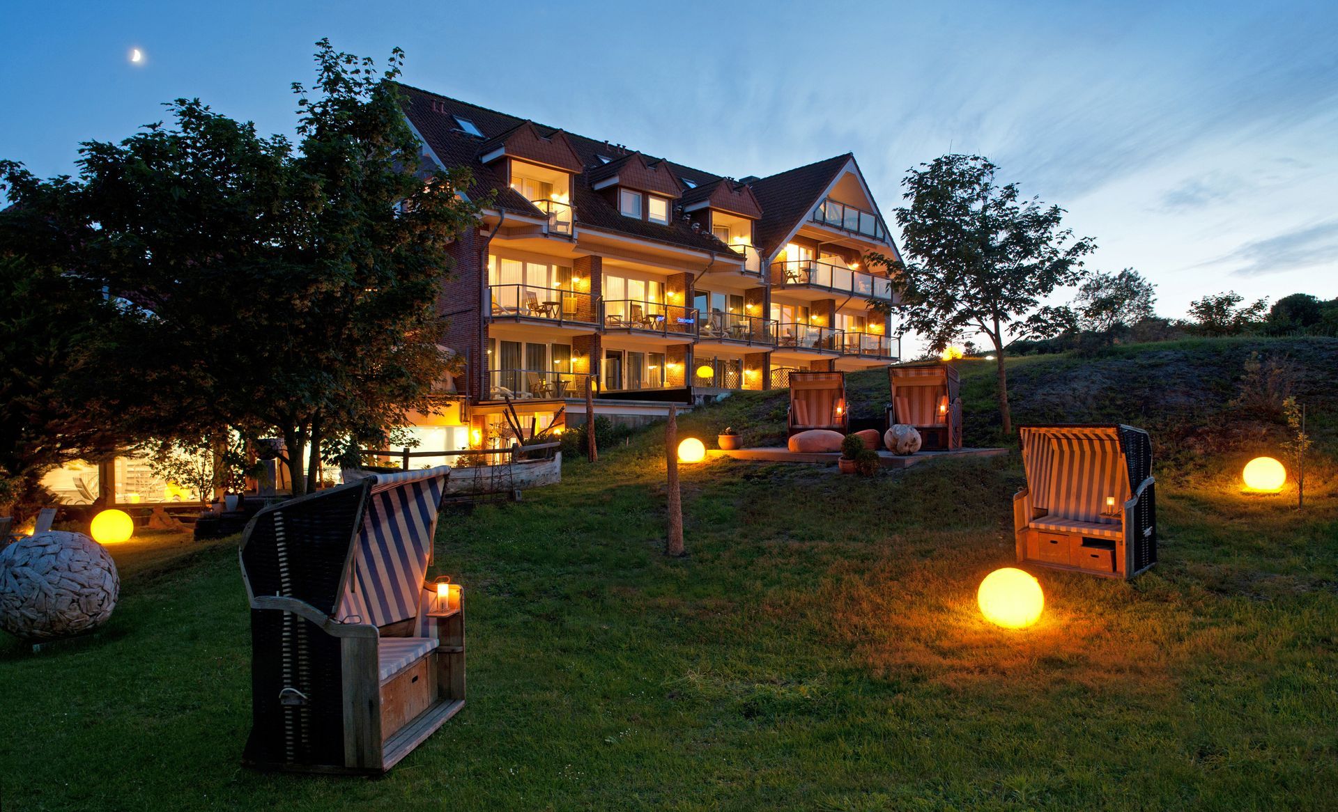 Hotel auf Juist am Abend, gemütlich beleuchtet mit Strandkörben auf der grünen Wiese.