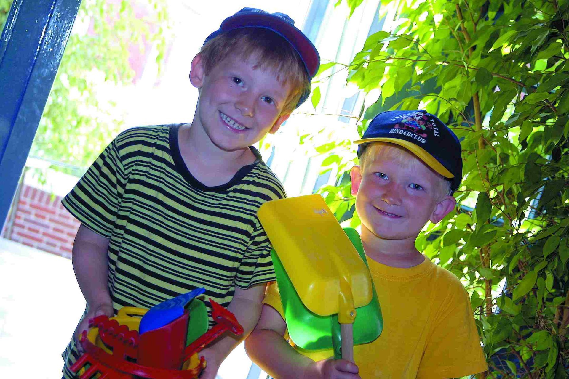 Zwei kleine Jungen stehen nebeneinander, halten Spielzeuge und lächeln.