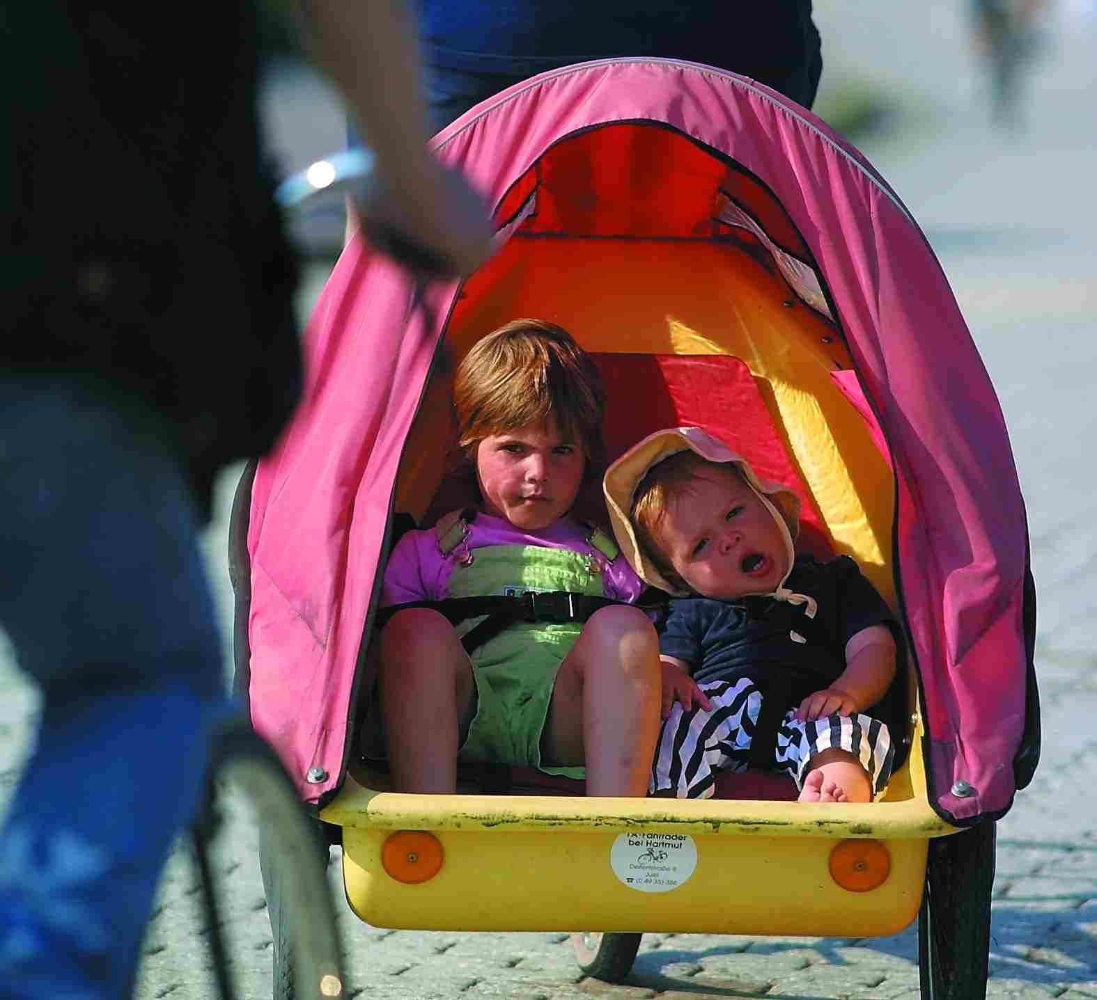 Zwei Kinder sitzen in einem Kinderwagen mit rosa Verdeck