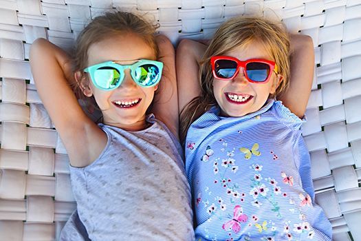 Zwei kleine Mädchen mit Sonnenbrillen liegen in einer Hängematte.