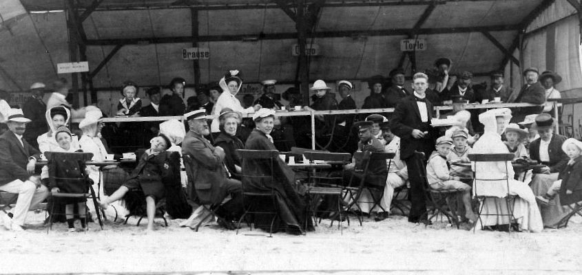 Ein Schwarzweißfoto einer Gruppe von Menschen, die an Tischen sitzen.