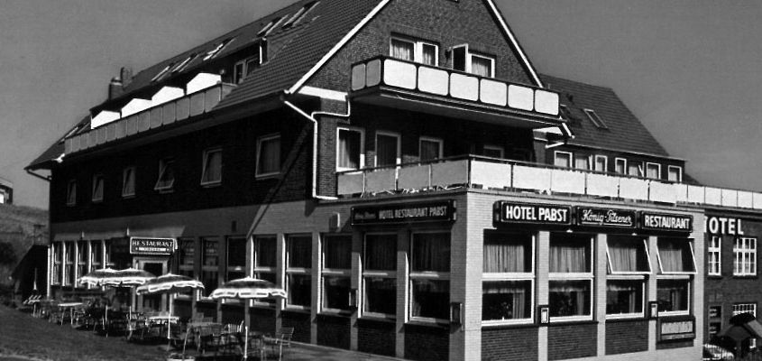 Ein Schwarzweißfoto eines Hotels mit Tischen und Stühlen draußen