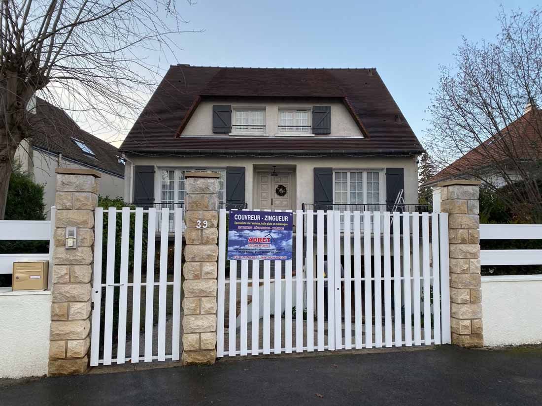 Portail blanc devant une maison au toit rénové